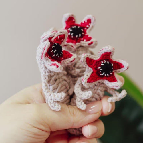 Hand holding a small crochet item with red and black flower patterns on a neutral background