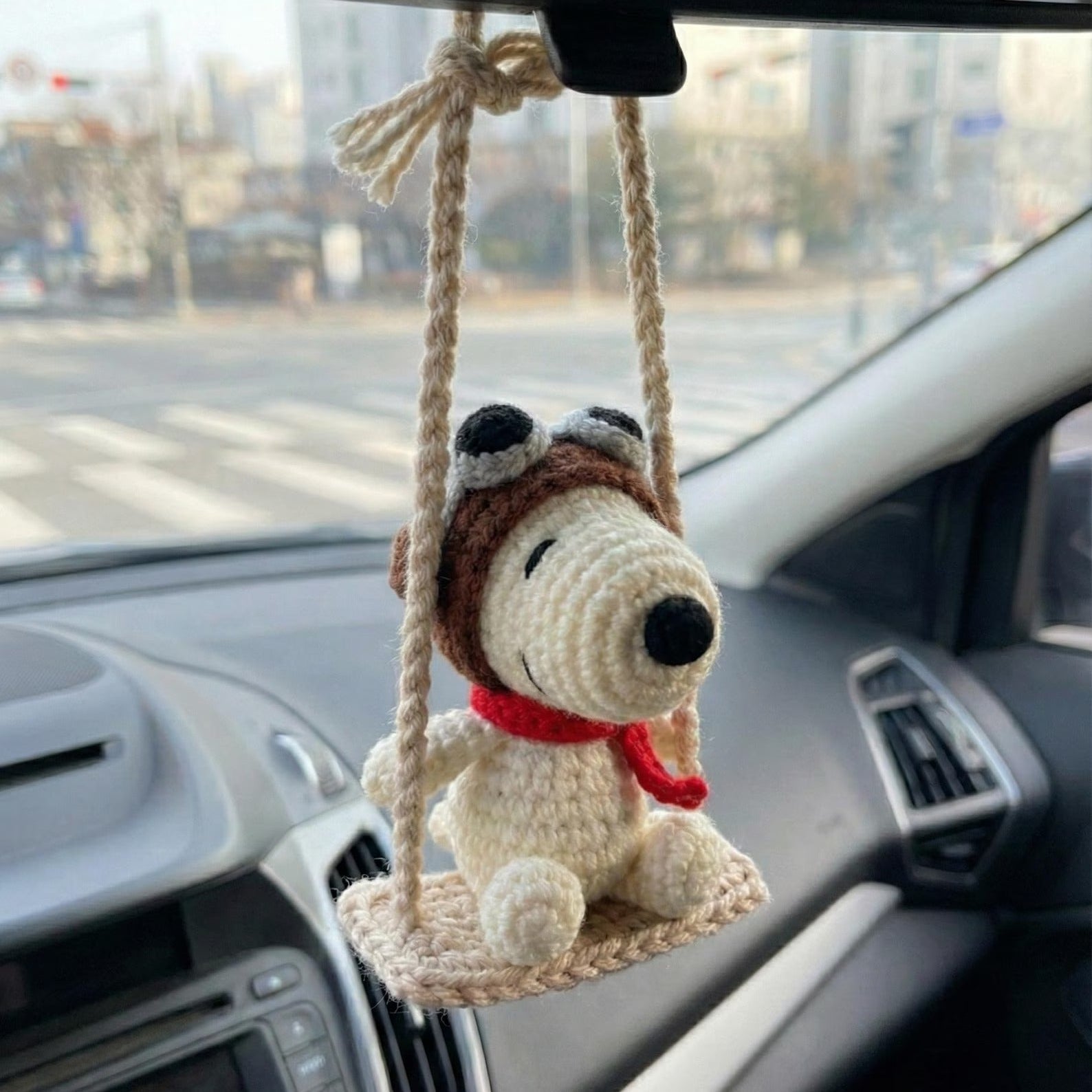 Crocheted dog toy on a swing hanging from a car's rearview mirror.