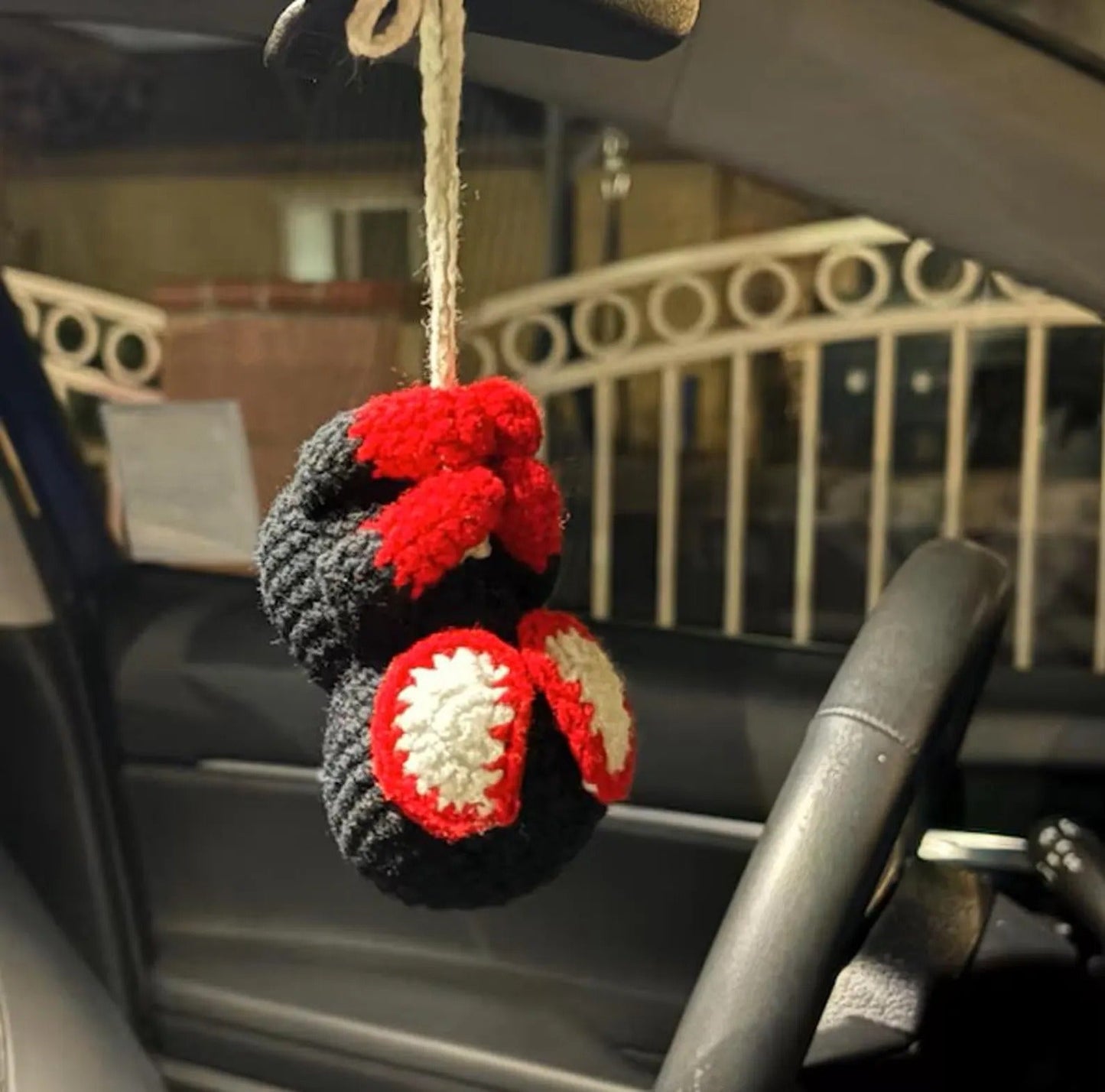 Crocheted keychain with red, white, and gray colors hanging from a car's rearview mirror.