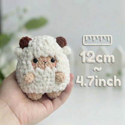 Small crocheted sheep toy held in a hand with measurement text on a light background
